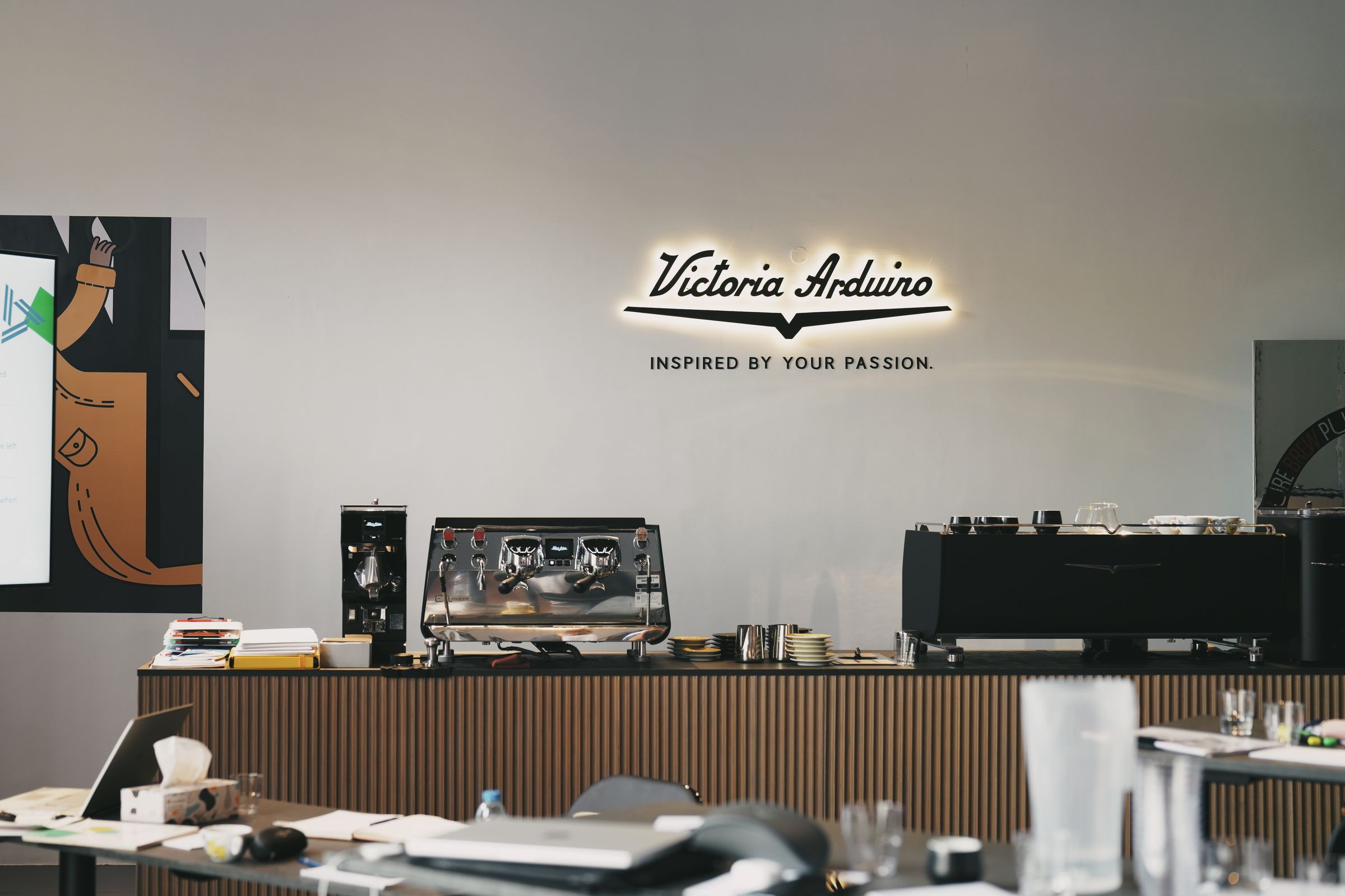 Illuminated Victoria Arduino sign above a bar with espresso machines and a grinder