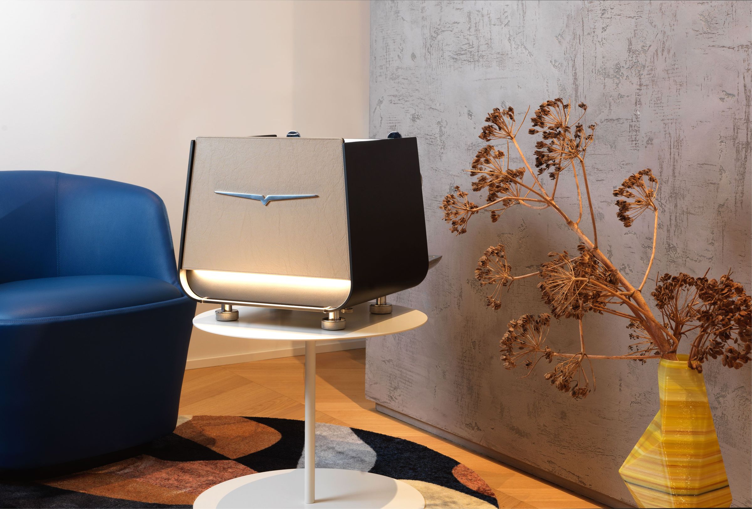 Victoria Arduino E1 Prima espresso machine on a round table next to a blue armchair